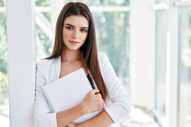 Belgeleri tutan ve modern yaratıcı ofiste kameraya bakan kendine güvenen bir iş kadını.