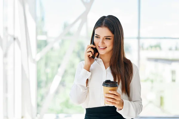 Lachende mooie zakenvrouw praten over de telefoon met een kopje koffie in de open ruimte modern kantoor — Stockfoto