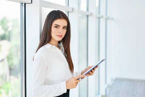 Selbstbewusst lächelnde Geschäftsfrau mit Klemmbrett in einem hellen modernen Büro — Stockfoto