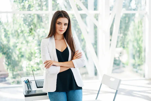 Sonriente mujer de negocios bastante segura con brazos cruzados posando en una oficina moderna — Foto de Stock