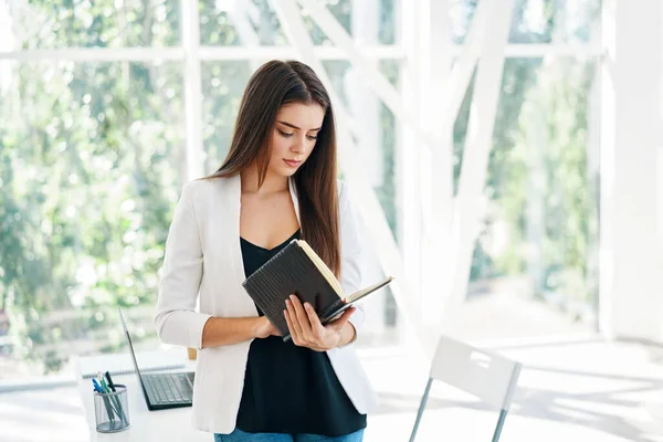 Портрет молодой красивой деловой женщины, читающей блокнот в современном креативном офисе — стоковое фото