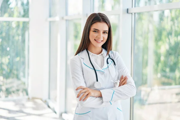 Joyeux médecin souriant avec les bras croisés dans le fond de l'hôpital — Photo