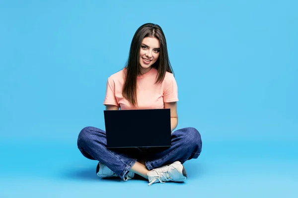 Portret van gelukkige jonge vrouw zitten op de vloer met benen gekruist werken op laptop — Stockfoto