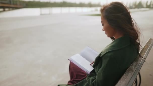 Młoda Azji kobieta czytanie książki siedzi na ławce w pobliżu rzeki — Wideo stockowe