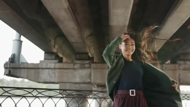 Feliz sorrindo asiático mulher girando ao ar livre sob ponte urbana — Vídeo de Stock