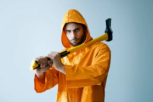 Joven hombre serio en impermeable brillante sosteniendo hacha grande en su hombro —  Fotos de Stock