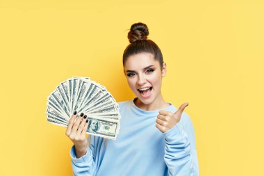 Mutlu, heyecanlı, genç bir kadın başparmaklarıyla para banknotları gösteriyor.