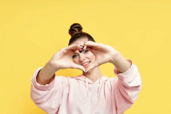 Young smiling pretty woman making heart symbol by hands on yellow background — Stock Photo, Image