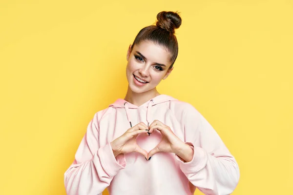 Jonge glimlachende mooie vrouw maken hart symbool door handen op gele achtergrond — Stockfoto