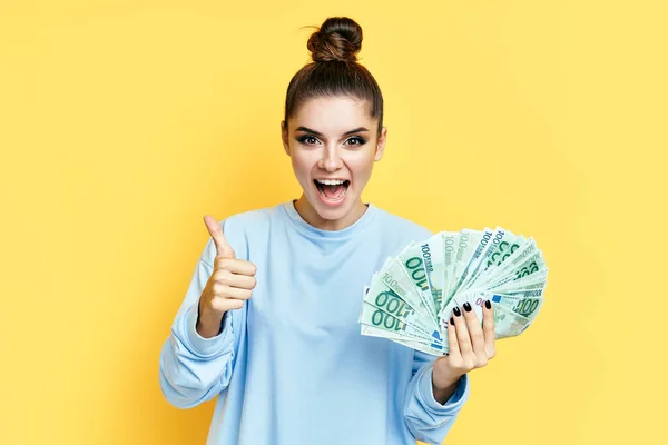 Happy excited young woman showing money banknotes with thumbs up — Stock Photo, Image