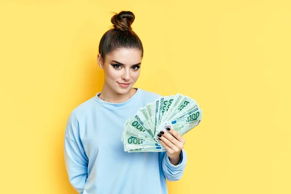 Ung söt kvinna som innehar pengar sedlar på gul bakgrund — Stockfoto