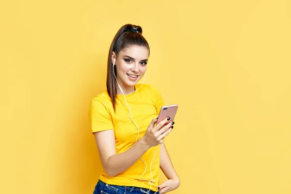 Mujer bastante caucásica escuchando música desde su teléfono y auriculares sobre fondo amarillo — Foto de Stock