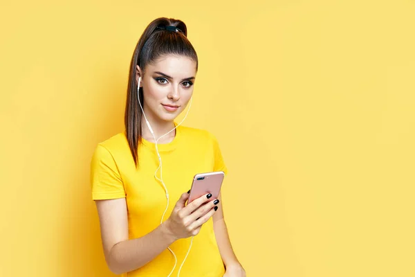 Mujer bastante caucásica escuchando música desde su teléfono y auriculares sobre fondo amarillo — Foto de Stock