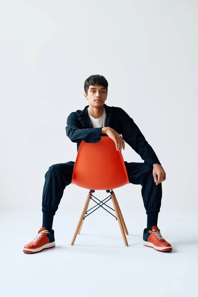 Elegante jovem bonito posando em estúdio sentado em uma cadeira olhando para câmera — Fotografia de Stock