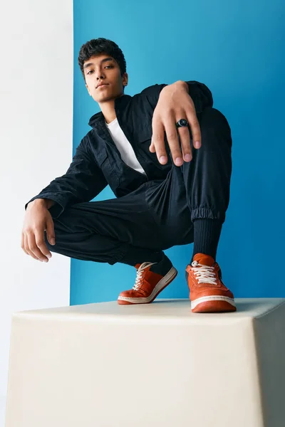 Fiducioso giovane uomo di razza mista alla moda in posa in studio seduto su un grande cubo — Foto Stock