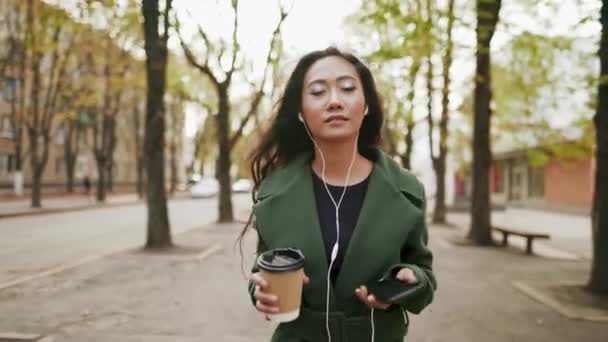 Elegante mulher asiática ouvir música com smartphone e beber café andando na rua — Vídeo de Stock