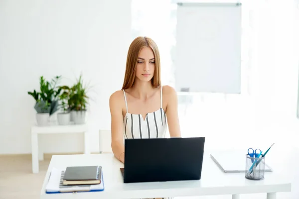 Piękna bizneswoman siedzi przy biurku i pracuje na laptopie w nowoczesnym biurze — Zdjęcie stockowe