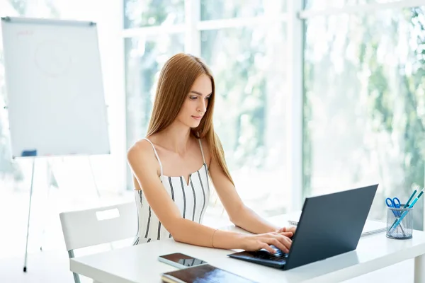 Красивая деловая женщина сидит за своим столом и работает на ноутбуке в современном офисе — стоковое фото