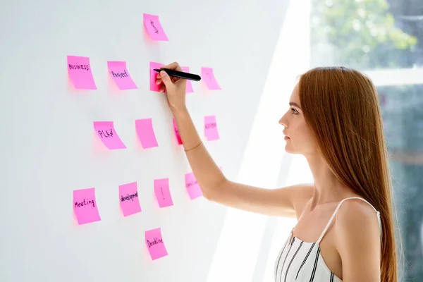 Atractiva mujer de negocios concentrada usando notas adhesivas para escribir y compartir ideas en la oficina creativa — Foto de Stock