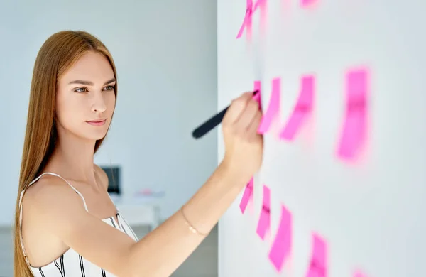 Attractive concentrated business woman using sticky notes to write and share ideas in creative office — Stock Photo, Image