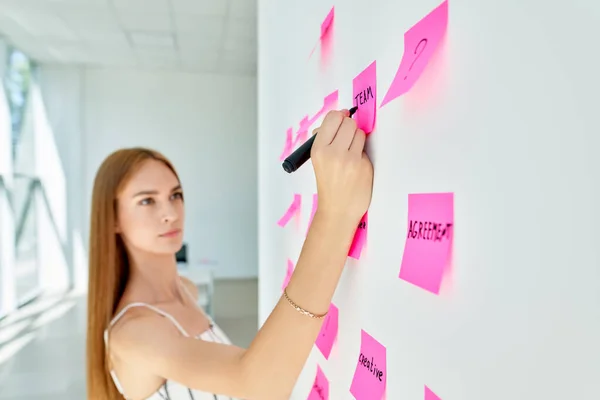 Atractiva mujer de negocios concentrada usando notas adhesivas para escribir y compartir ideas en la oficina creativa — Foto de Stock