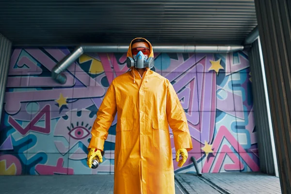 Graffiti pintor en máscara respiradora de pie cerca de la pared con sus pinturas —  Fotos de Stock