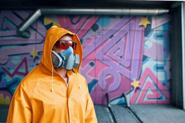 Graffiti painter in respirator mask standing near the wall with his paintings