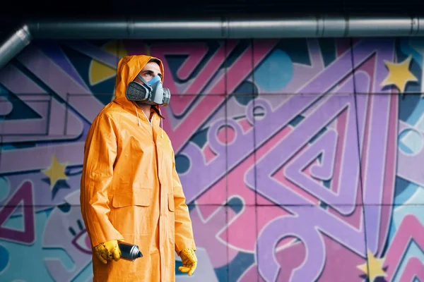 Graffiti pintor en máscara respiradora de pie cerca de la pared con sus pinturas —  Fotos de Stock