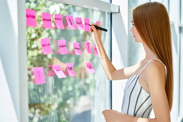 Atractiva mujer de negocios confiada usando notas adhesivas para escribir y compartir ideas en la oficina creativa — Foto de Stock