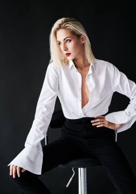 Siyah stüdyo arka planında sandalyede poz veren şık bir kadın.