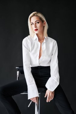 Siyah stüdyo arka planında sandalyede poz veren şık bir kadın.