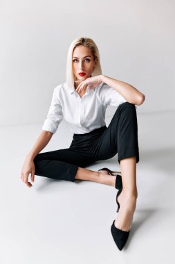 Beyaz stüdyo arka planında poz veren moda bir kadının portresi. Yerde oturuyor.