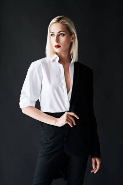 Klasik erkek kıyafeti giyen şık bir kadın siyah stüdyo arka planında poz veriyor.