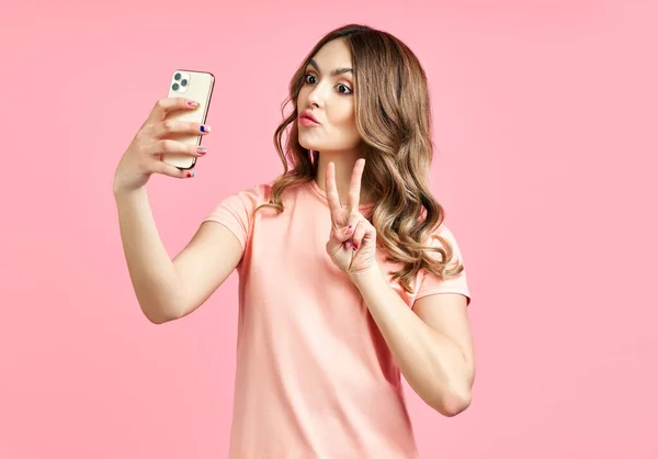 Encantadora chica hermosa haciendo retrato de selfie en el teléfono inteligente haciendo V signo de mano — Foto de Stock