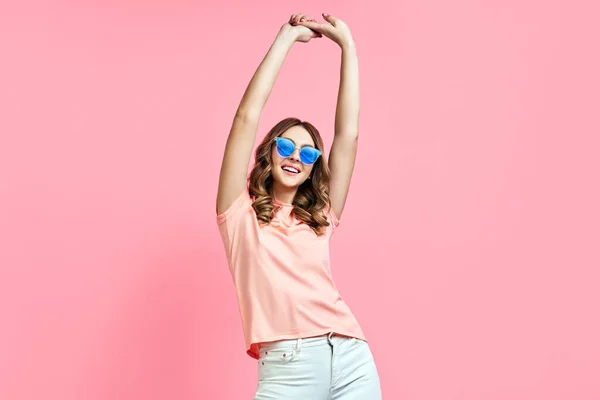 Mujer con estilo feliz en gafas de sol fresco con las manos arriba posando en rosa —  Fotos de Stock