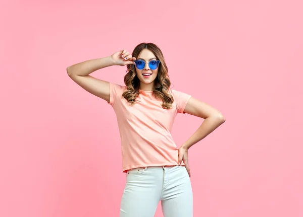 Mujer joven con estilo en gafas de sol azules sonriendo y posando en rosa —  Fotos de Stock