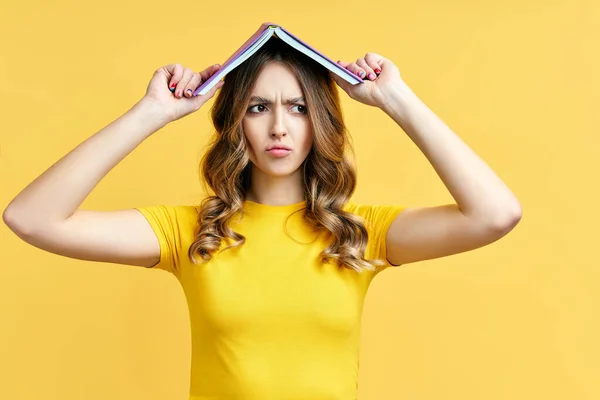 Zdjęcie śmiesznej kobiety trzymającej książkę nad głową, zdezorientowany wyraz twarzy — Zdjęcie stockowe