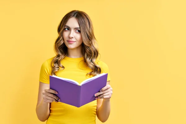 Sonhador positivo menina resto com livro no fundo amarelo com espaço de cópia — Fotografia de Stock