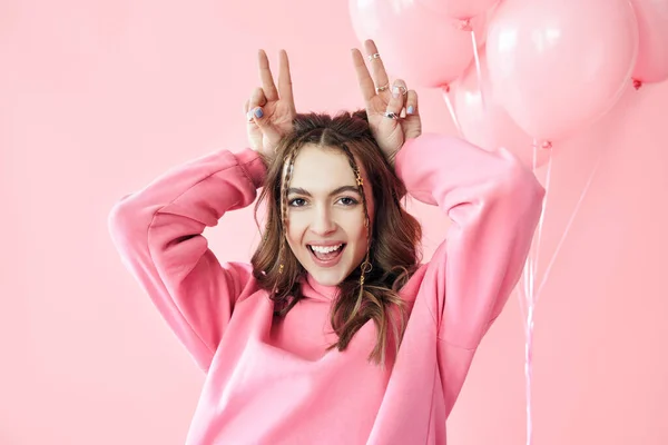 Jovem mulher bonita se divertir mostrando chifres com os dedos sobre a cabeça no fundo rosa — Fotografia de Stock