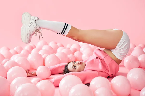 Νεαρή όμορφη γυναίκα έχουν τη διασκέδαση με τα πόδια επάνω που βρίσκονται σε ροζ μπαλόνια πάνω από ροζ παστέλ φόντο — Φωτογραφία Αρχείου