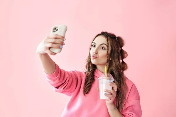Joven mujer de moda haciendo retrato selfie sosteniendo batido sobre fondo rosa — Foto de Stock