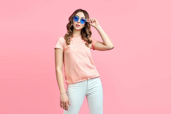 Trendy young woman in blue sunglasses posing over pink background — Stock Photo, Image