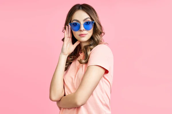 Trendige junge Frau mit blauer Sonnenbrille posiert vor rosa Hintergrund — Stockfoto