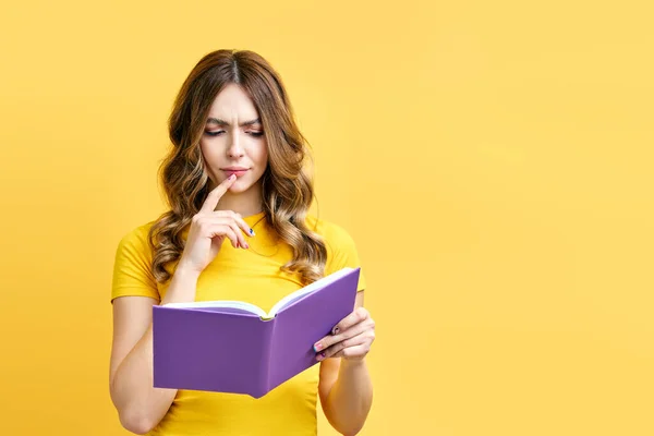 Jovem mulher pensativa sério ler livro no fundo amarelo com espaço de cópia — Fotografia de Stock