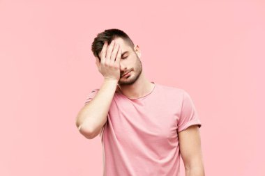 Tired disappointed young man with face palm gesture over pink background clipart