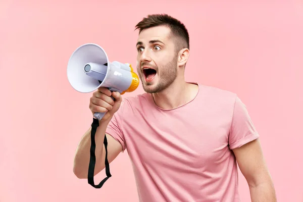 Забавный молодой человек кричит громко держа мегафон на розовом фоне — стоковое фото