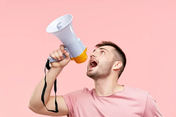 Engraçado jovem gritando alto segurando um megafone sobre fundo rosa — Fotografia de Stock