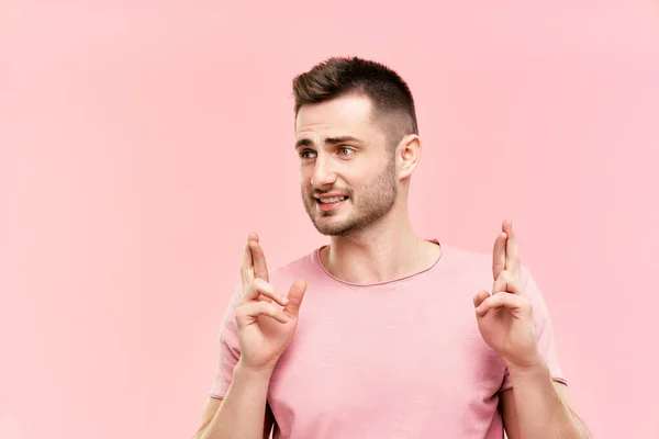 Молодой красивый мужчина скрещивает пальцы и желает удачи на розовом фоне — стоковое фото