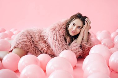 Bir sürü pembe balonun içinde yatan gülümseyen güzel bir kadının moda portresi.