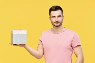 Sarı stüdyo arka planında hediye kutusu tutan yakışıklı genç adam.